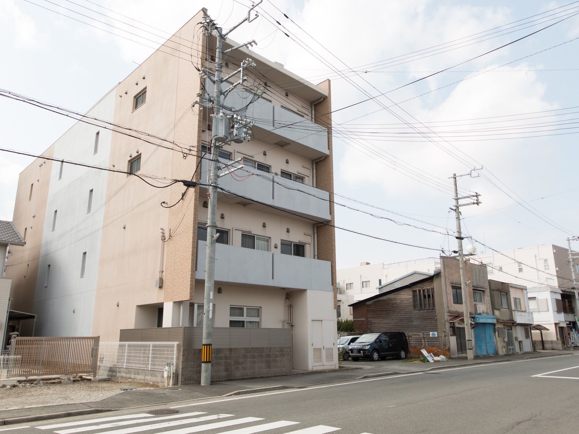 大きな道路が施設の前を通っている。大きなベランダが備わっている。鉄筋コンクリート造りの４階建てである。