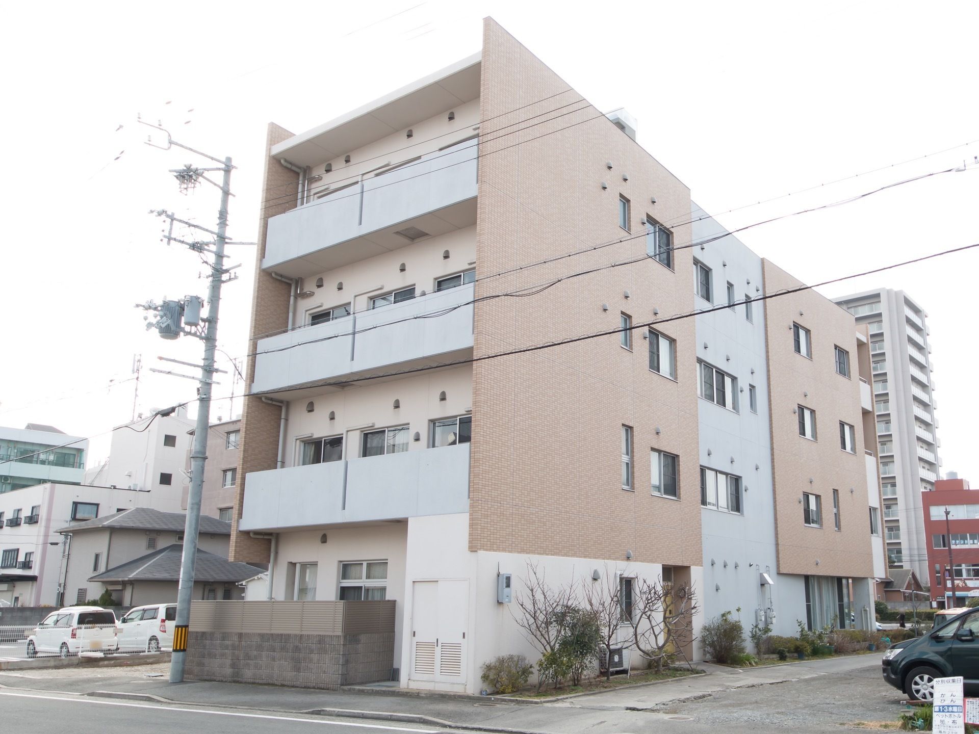 道路に面した４階建ての、窓が多い建物である。建物のすぐそばに建物と同じ高さの電柱があり、横には駐車スペースもある。