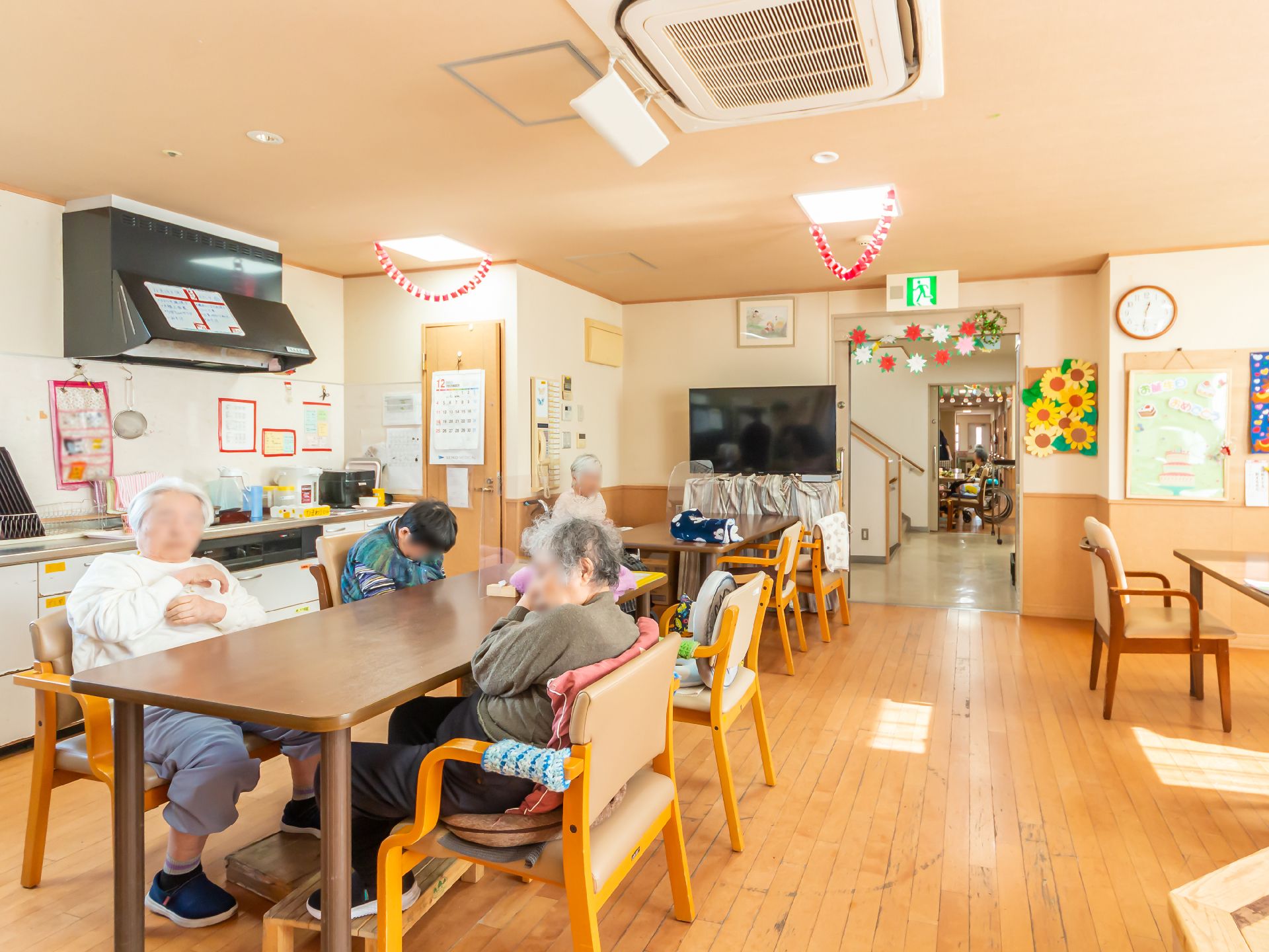 夏祭りの様子。ちょうちんなどが飾られた屋外にはテーブルセットが複数並べられ、ハッピを着たスタッフが食事の介助などをしている。