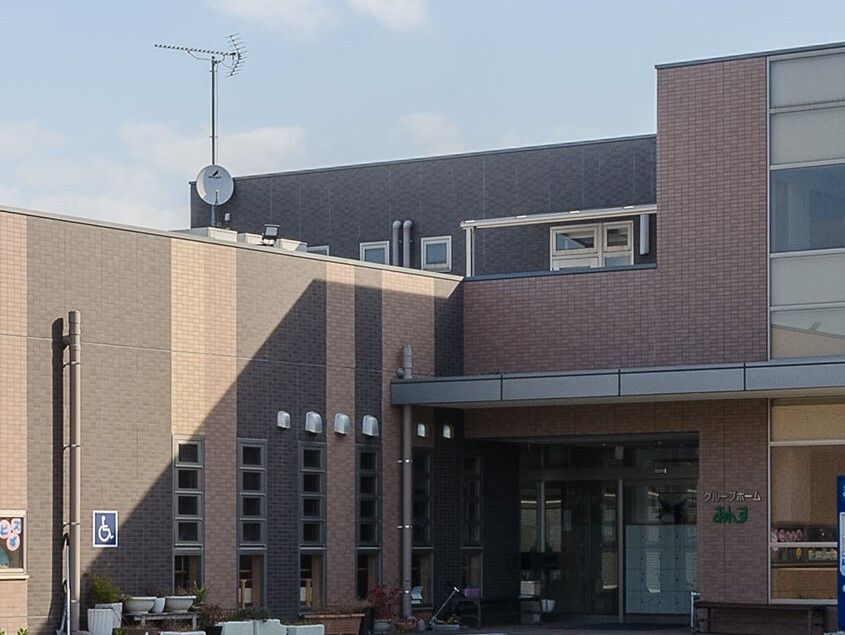 ブラウン系の建物の玄関には屋根があり、玄関の周りにはプランターがたくさん置かれている。