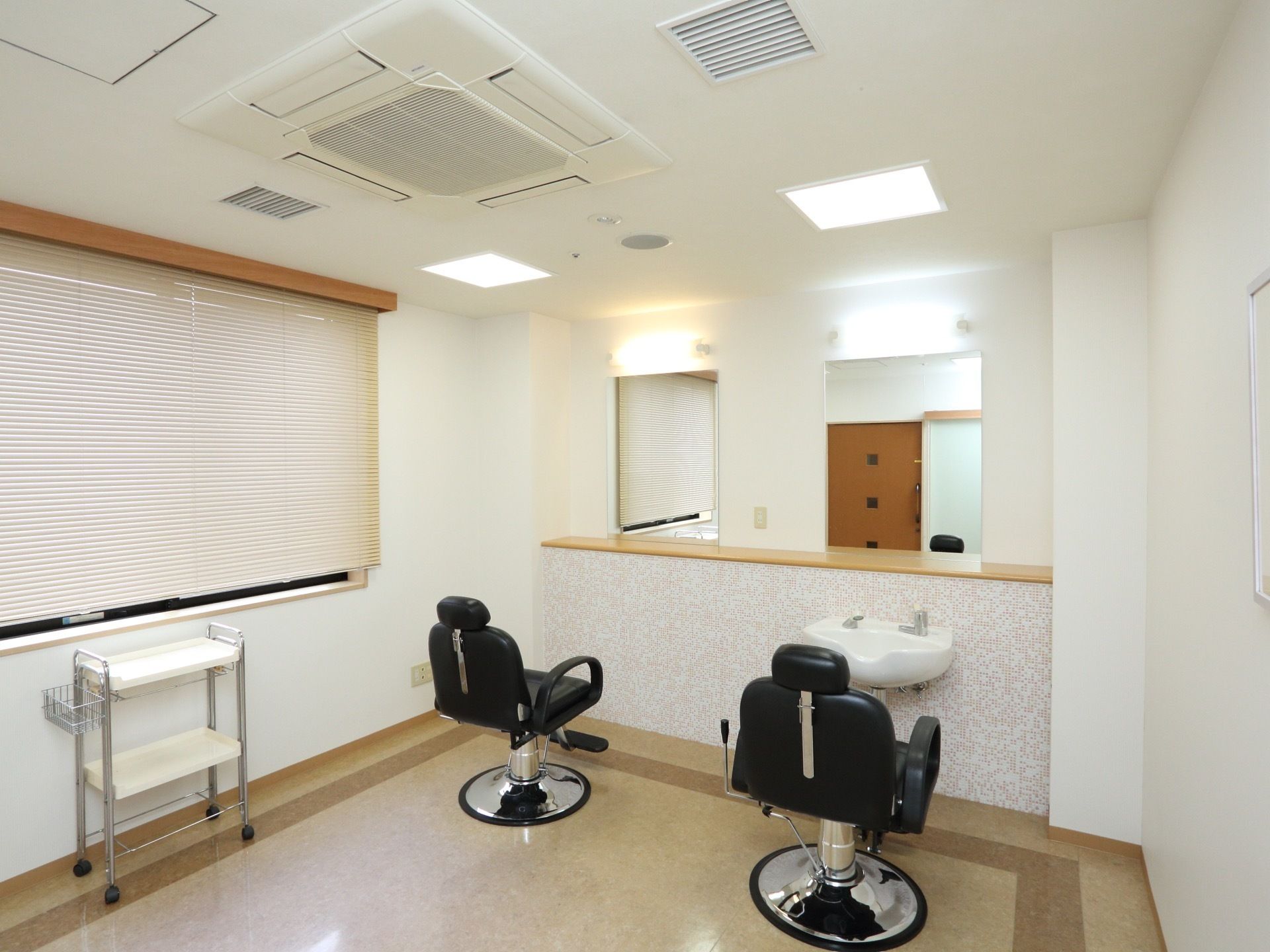 施設内に美容室がある。大きな２枚の鏡の前に２台の椅子が設置されている。そのうち一台の前には、洗面台がある。
