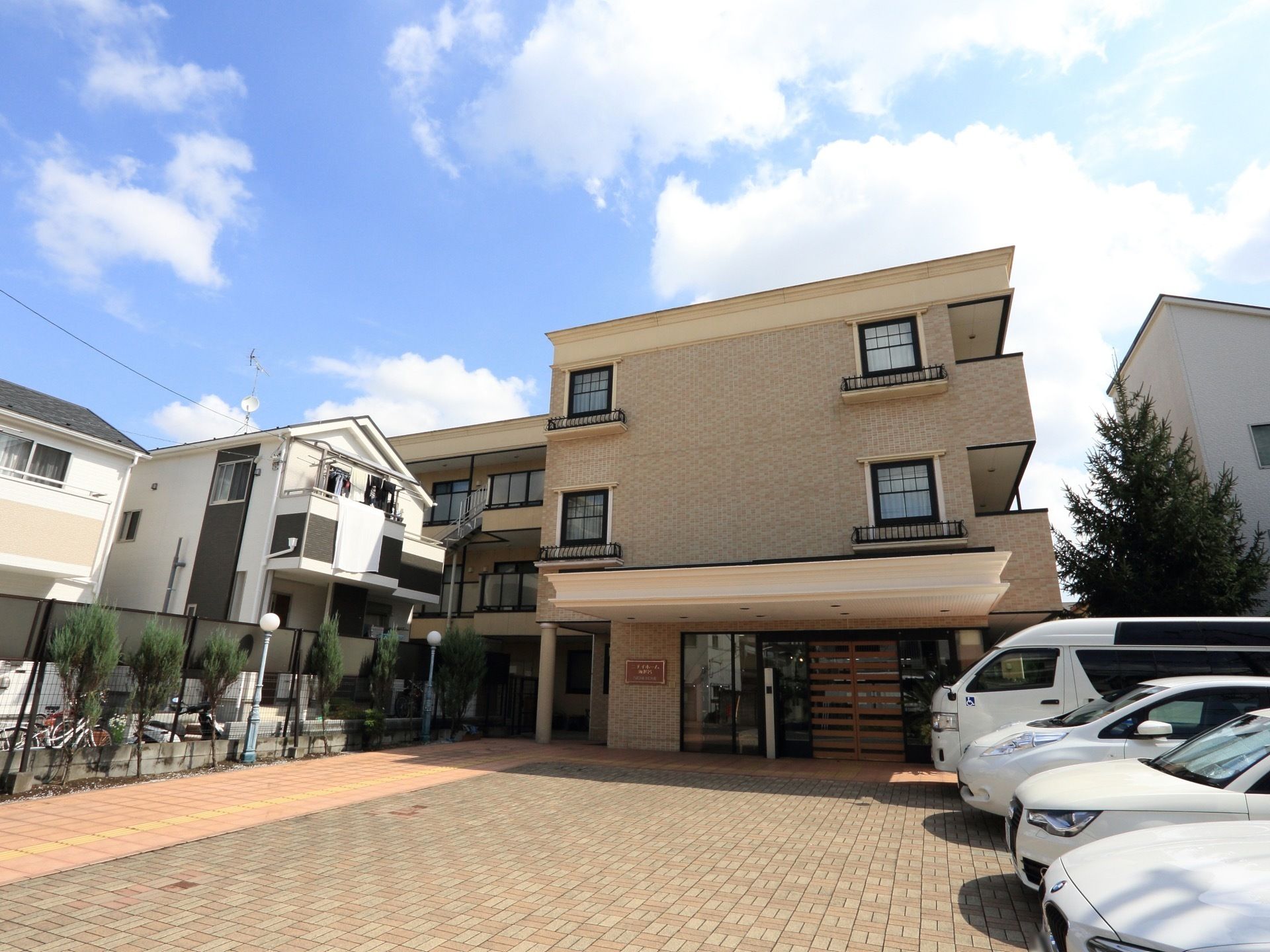 落ち着いた色調の３階建ての施設である。玄関の目の前には広い駐車スペースがある。周囲には一般住宅が建っている。