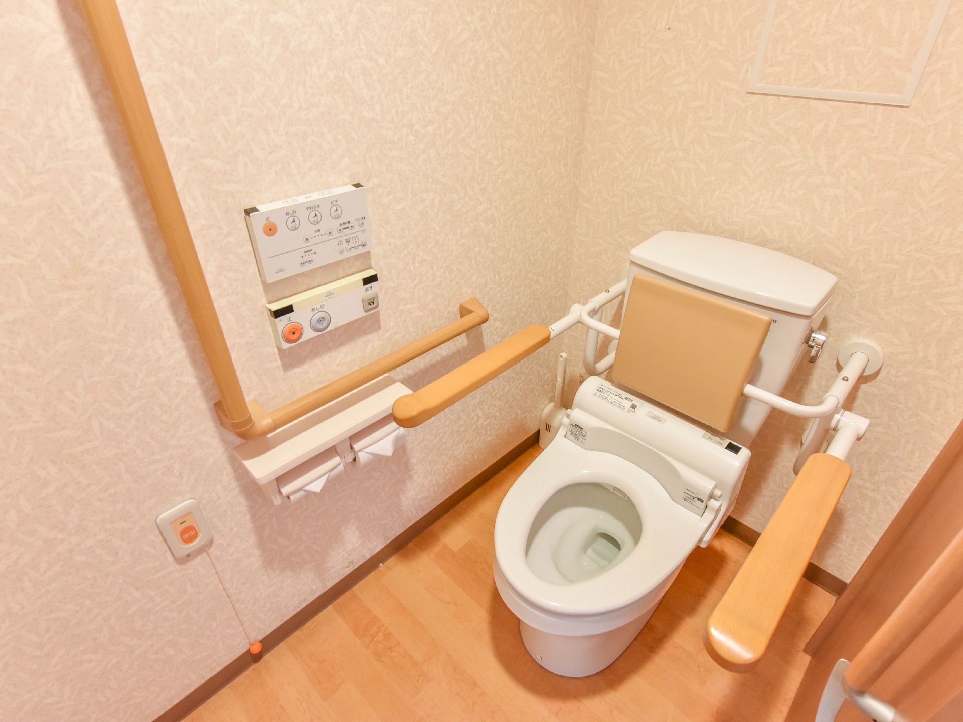 白が基調の明るいトイレには、座った時のクッションになる背もたれや立ち上がりや座る時の支えになるバーが完備されている。
