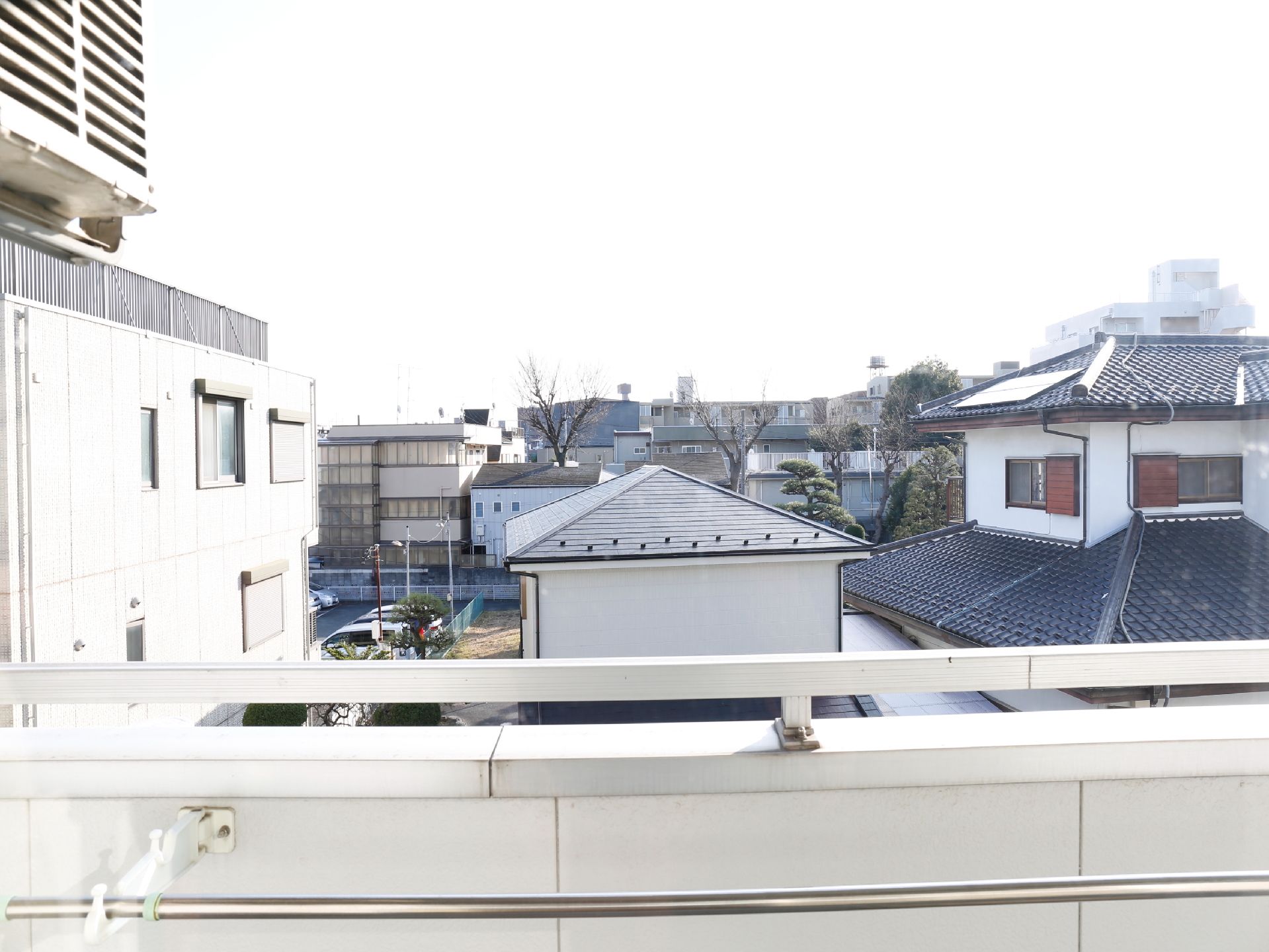 白壁のベランダからは住宅街の町並みが見える。ベランダには物干し竿が設置されている。高いビルなどは無いので見晴らしが良い。