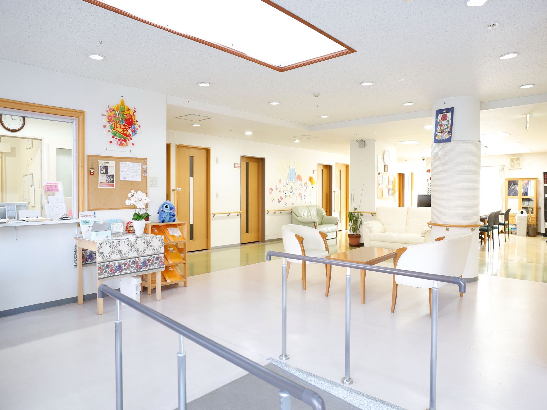 受付前のホールは壁床天井すべて白を基調としており清潔感がある。椅子やテーブル、リハビリ用の平行棒なども設置されている。
