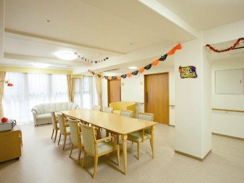 アイボリーの椅子とソファーを設置したスペースは、入居者様が共用している。天井にぶら下げたモールなどの飾りで部屋にカラーをプラスしている。