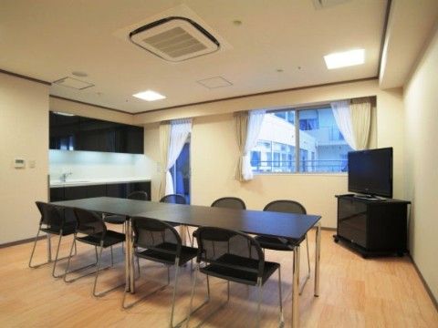 窓際にはテレビとキッチンスペースがあり、部屋の中央には黒いテーブルと8脚の黒い椅子が並べられている。