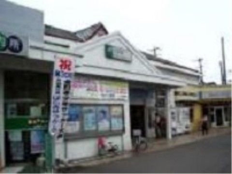 白い外観の駅舎がある。入口の横側には大きな掲示板があり、複数枚の紙が貼り付けられている。掲示板の横には旗が掲げられている。