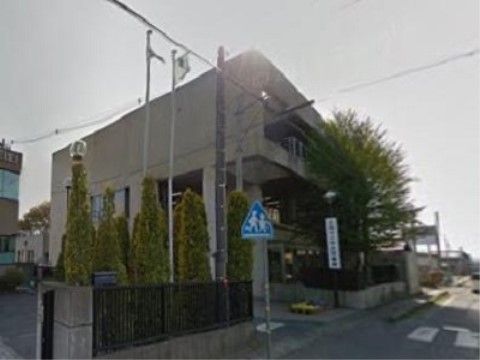 道路に面した場所に四角い建物の図書館がある。通学路になっており、子どもが横断歩道を渡っている標識が設置されている。