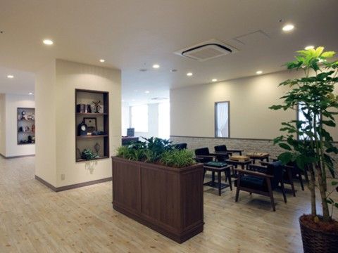 落ち着いた雰囲気のラウンジである。テーブルと椅子のセットが用意されている。観葉植物が置かれている。柱には、飾り棚が設けられている。
