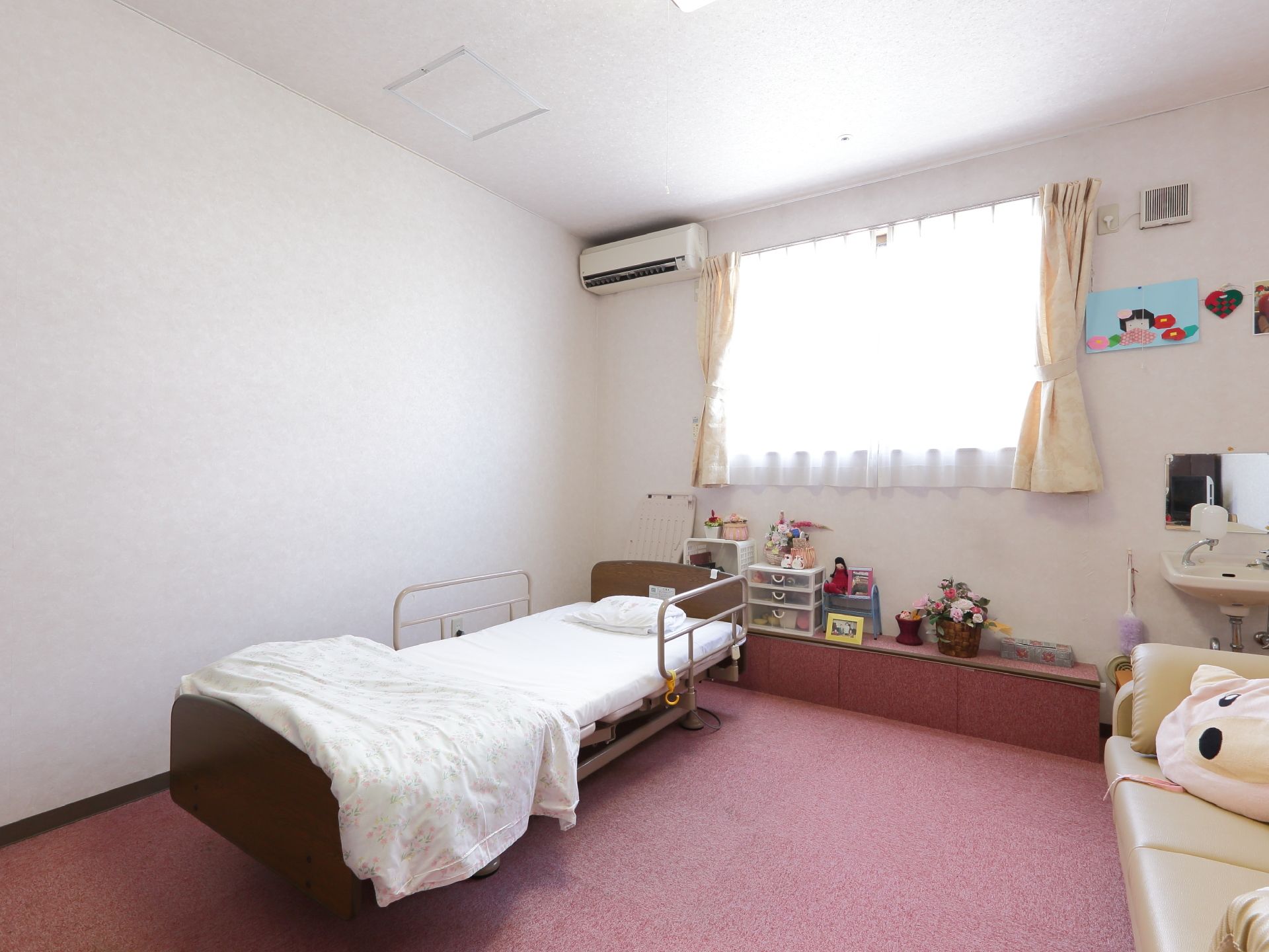 窓際の壁に洗面台と鏡、エアコンがある。小物や花等を綺麗にレイアウトしてある。ベッドには落下防止の柵が付いている。