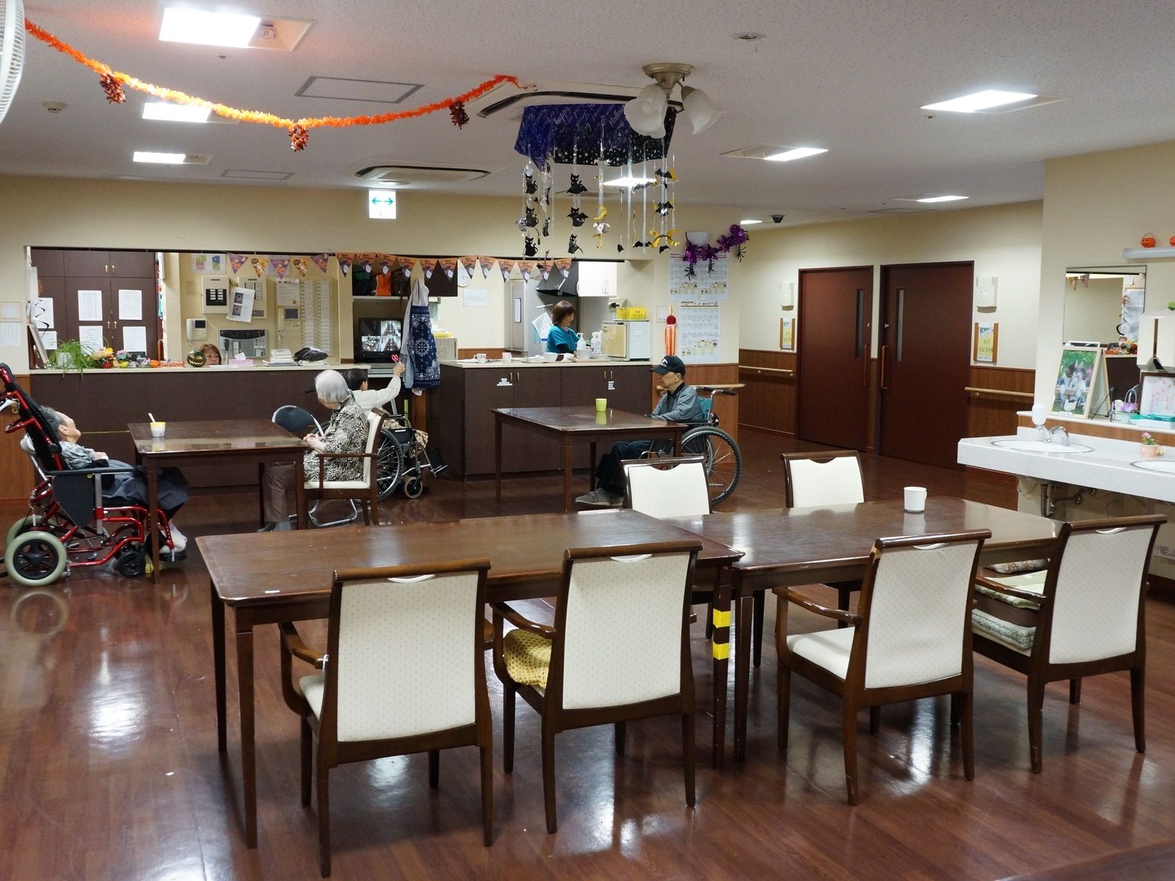 飾りが飾られている共有スペースには、車いすに乗っている入居者様もいる。奥ではそんな人たちのためにスタッフが何らかの準備をしている。