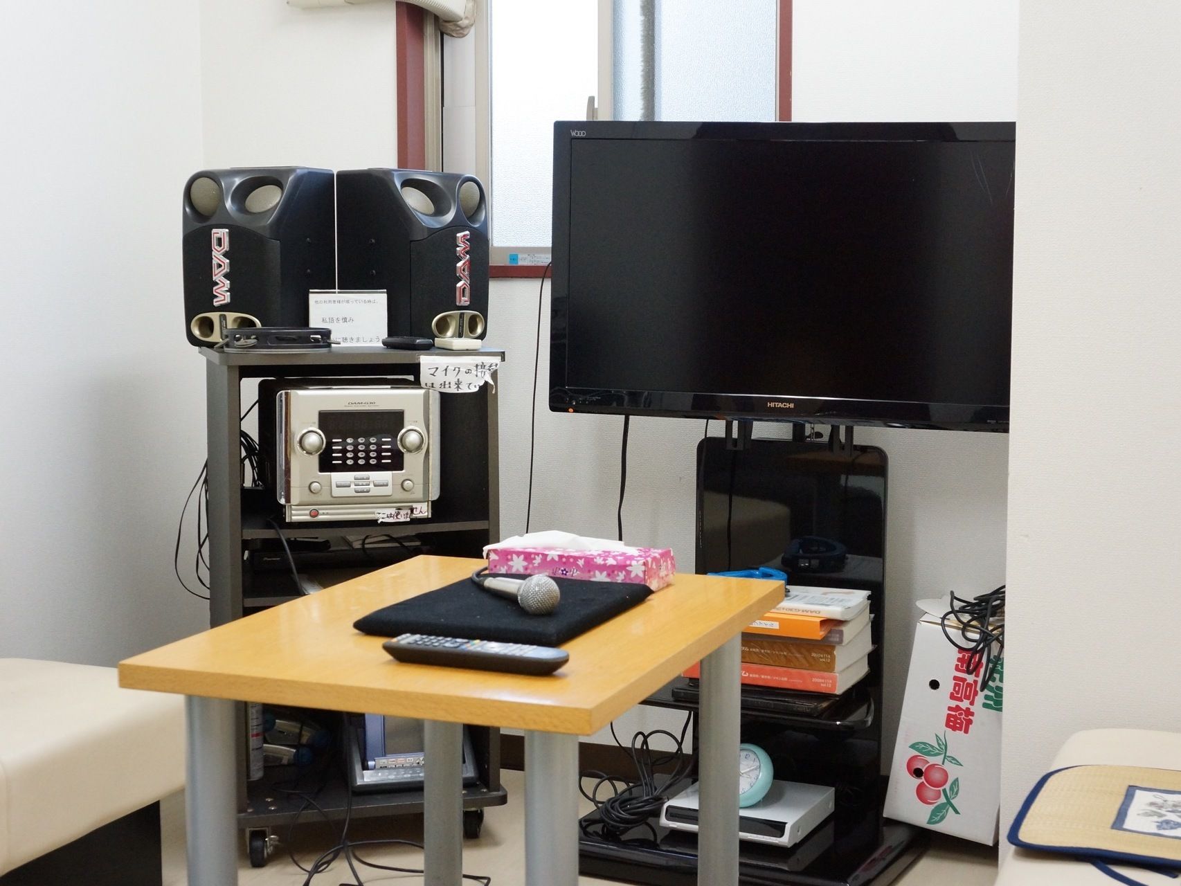 部屋の片隅には、入居者様が楽しめるようテレビとカラオケ機器が置いてある。テーブルにはマイクやリモコン、選曲用の本などが置いてある。