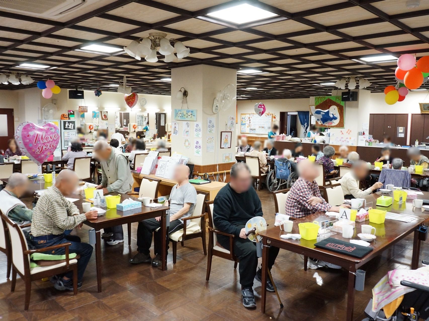 共有スペースにはたくさんの入居者様が座っており、飲み物などを飲んでくつろいでいる。部屋の中にはハート型の風船があり華やかになっている。