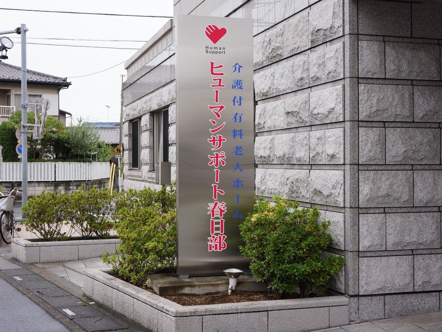 施設の入り口部分には銀色に青文字と赤文字の、施設名の入った看板があり、観葉植物の間に目立つ形で置かれている。