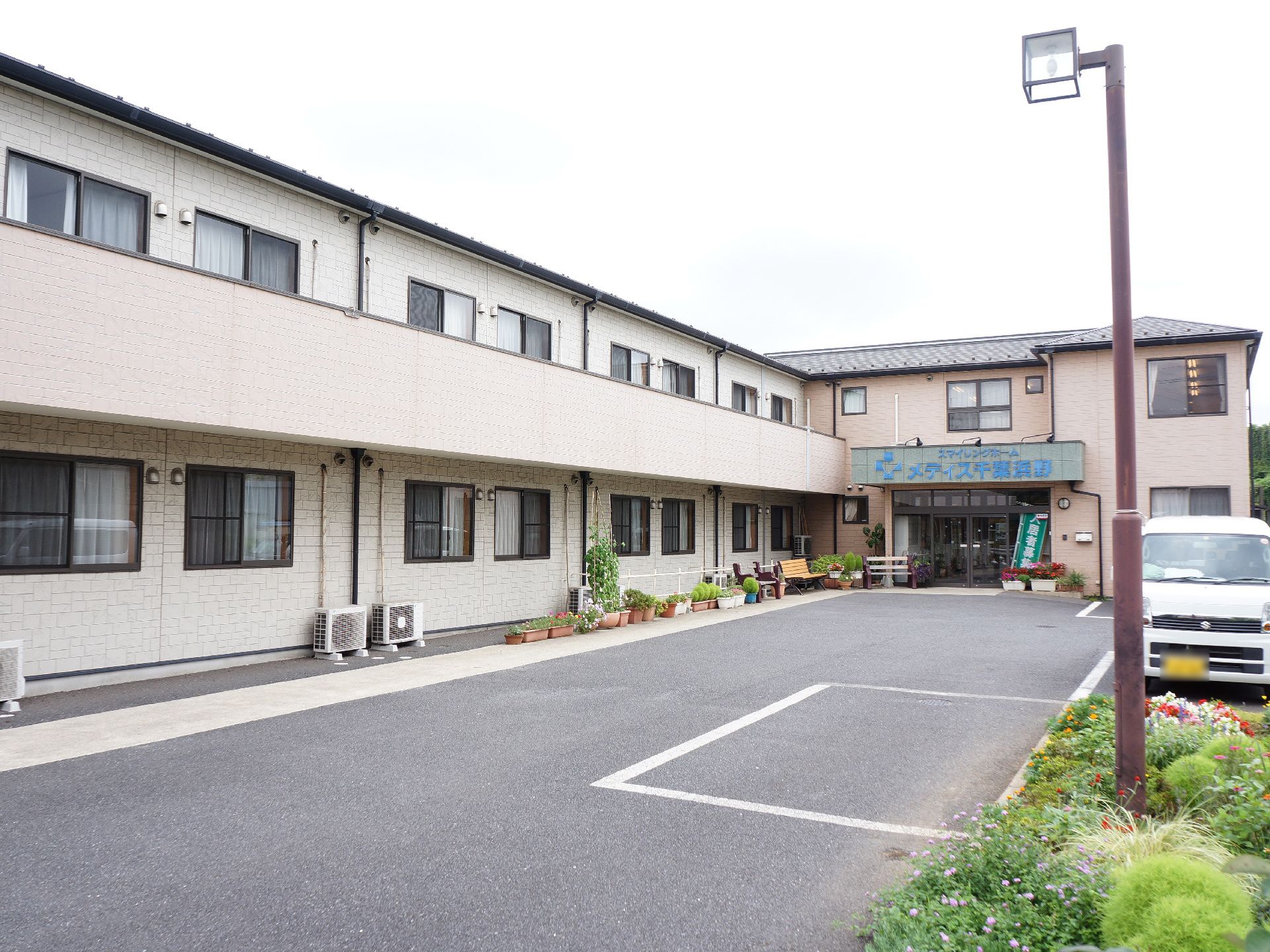 広い敷地に2階建てで施設の建物が建てられている。正面玄関の上には施設名が青字で大きく書かれた看板がある。