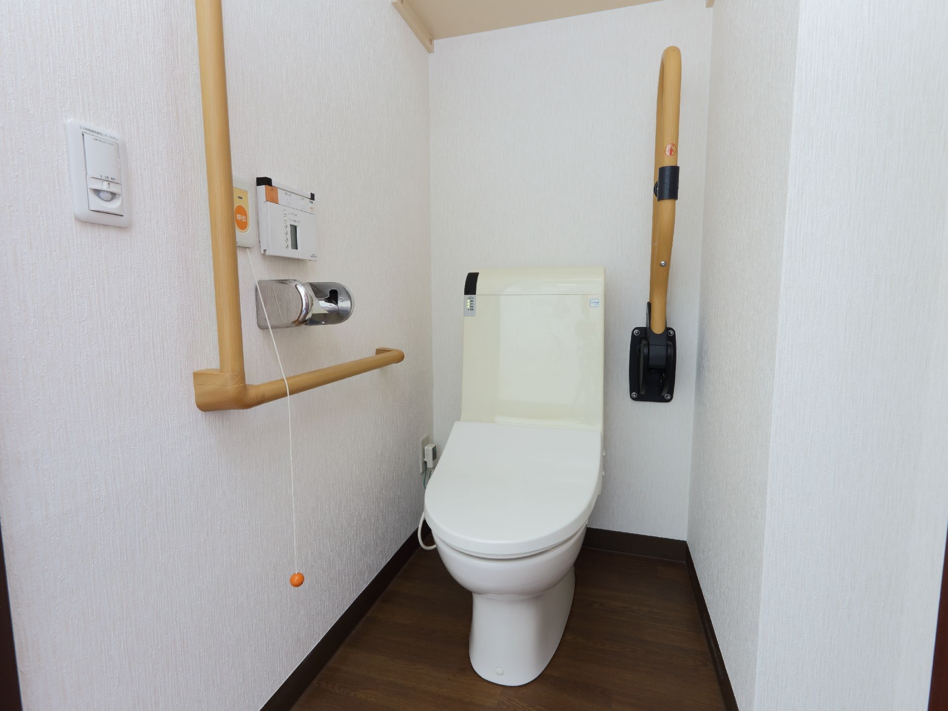 室内には、タンク付きのトイレが設置されている。トイレの両側にはベージュ色の手すりも取りつけられている。