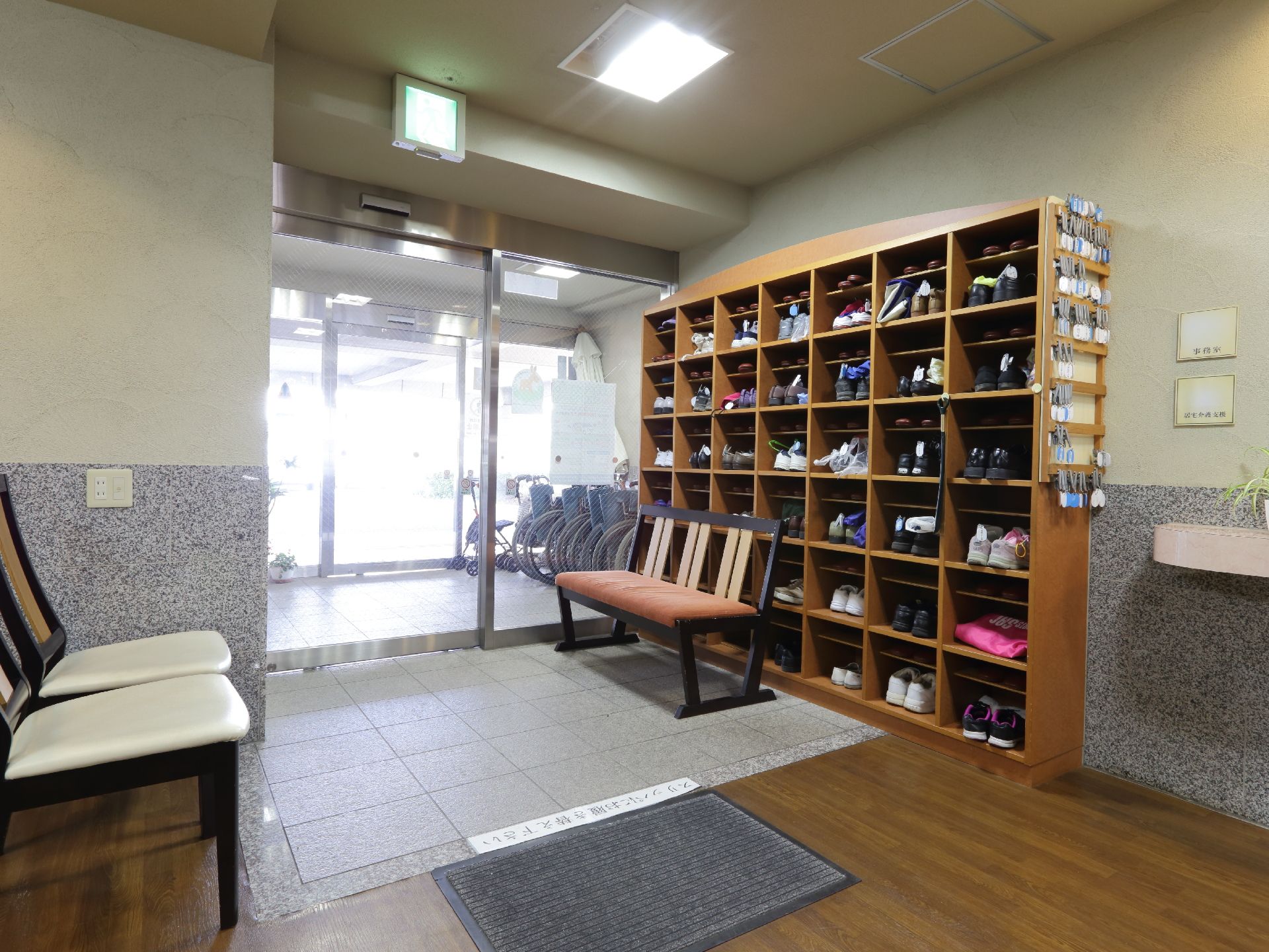 二重扉から中に入れば、壁際に靴箱が設置。その前には、2、3人掛けの背もたれの椅子が置かれている。上り口は段差がなくマットが敷かれている。