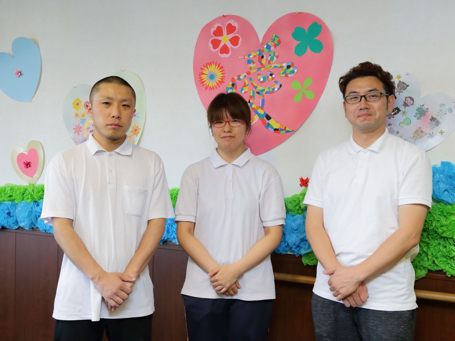 手作りの装飾品が飾られている壁をバックに並んでいる、三人のスタッフたち