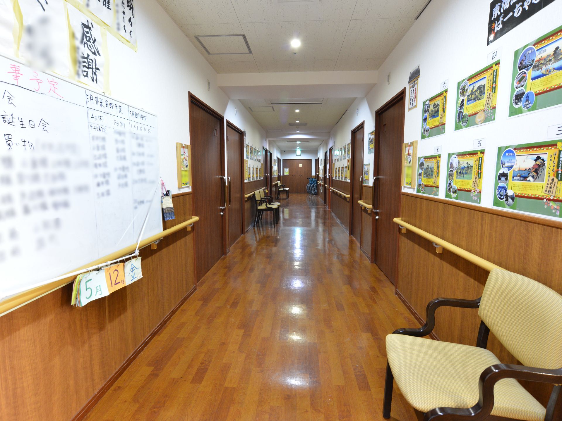明るいi廊下に、椅子がいくつか配置されている。壁には予定表や利用者様のお習字の作品が展示されている。
