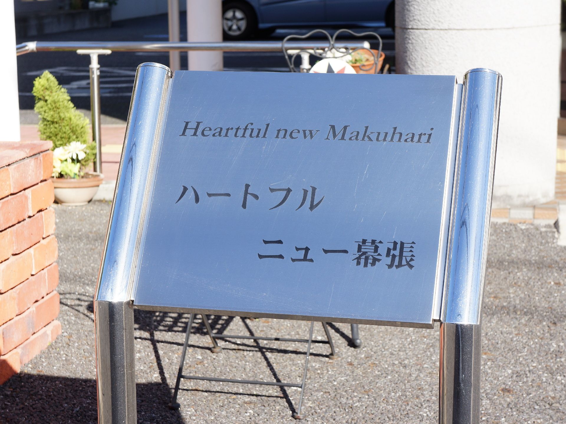 施設の外に看板が置いてある。ステンレス製の大きな看板でアルファベットと片仮名で表記してあり目立っている。