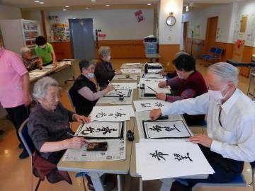 テーブルに向かい合って座り、書道を楽しむ入居者たちとスタッフ