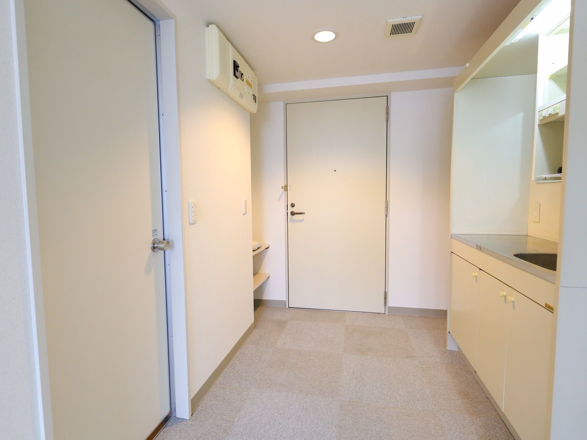 居室入口の扉は、取っ手がついた白い開き戸である。入ってすぐの所にキッチンが設置されている。その反対側の壁の上にブレーカー盤が見える。
