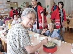 外部の人と会話しながらたこ焼きを作っている高齢者。笑顔で振り向いている