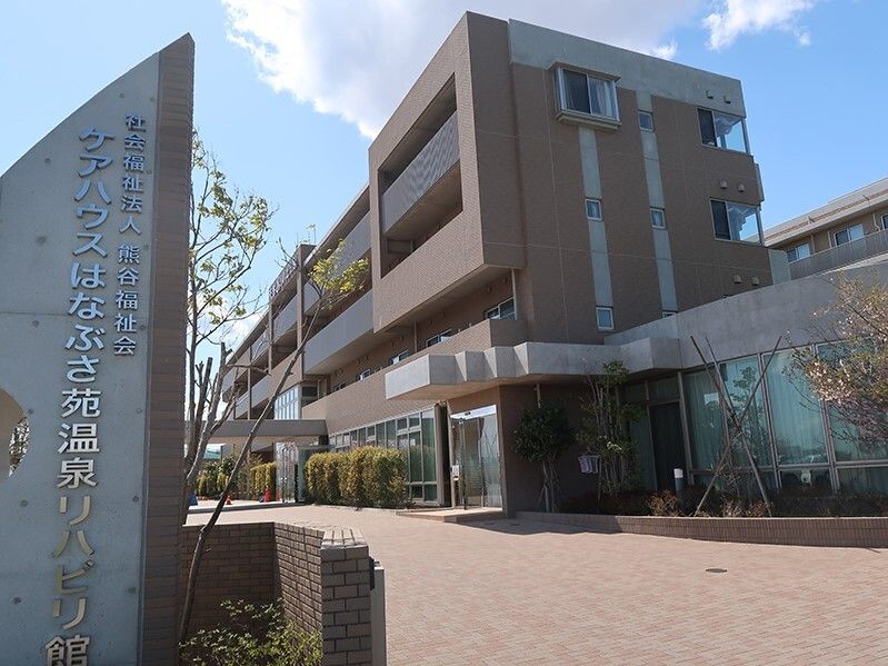 ブラウン系の建物の各フロアにベランダが付き、玄関先には屋根があり、敷地は広く、緑もたくさん植えられている。