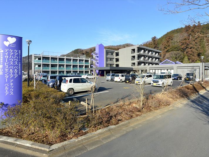 広い駐車場にはたくさんの車が止まっていて、館銘板の周りには草木が植えられている。3階建ての建物と4階建ての建物がある。