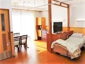 ベッドとリビング部分に仕切りがある広めの部屋の様子。施設内の居室の写真