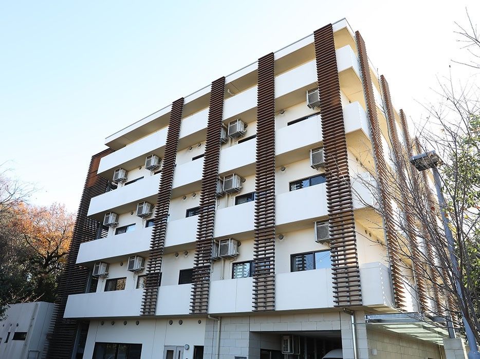 緑に囲まれた白とブラウンの大きな建物。各フロアにはベランダがあり、日当たりもよい。
