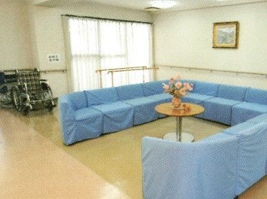 ブルーのコの字型のソファの中央には花が生けられたテーブルがあり、奥には平行棒もある。