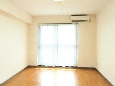 シンプルなエアコン付きのフローリングの居室。窓にはカーテンが付いている。