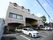 建物中央の奥まった場所に玄関があり、上には大きな屋根が付いている。建物の前には駐車場が設けられ、車が数台停まっている。