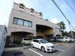 建物中央の奥まった場所に玄関があり、上には大きな屋根が付いている。建物の前には駐車場が設けられ、車が数台停まっている。