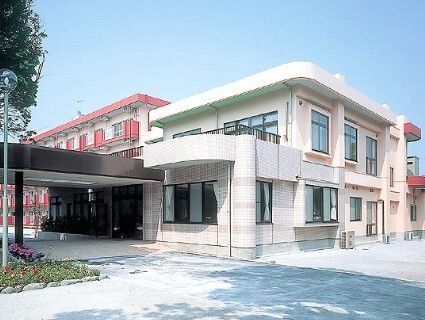 白を基調とした２階建て建物が手前にあり、奥には白と濃いピンクの建物がある。