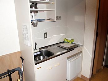 部屋のキッチンはIHクッキングヒーターが付いたオール電化の仕様。キッチンの横には杖や歩行器が置かれている。