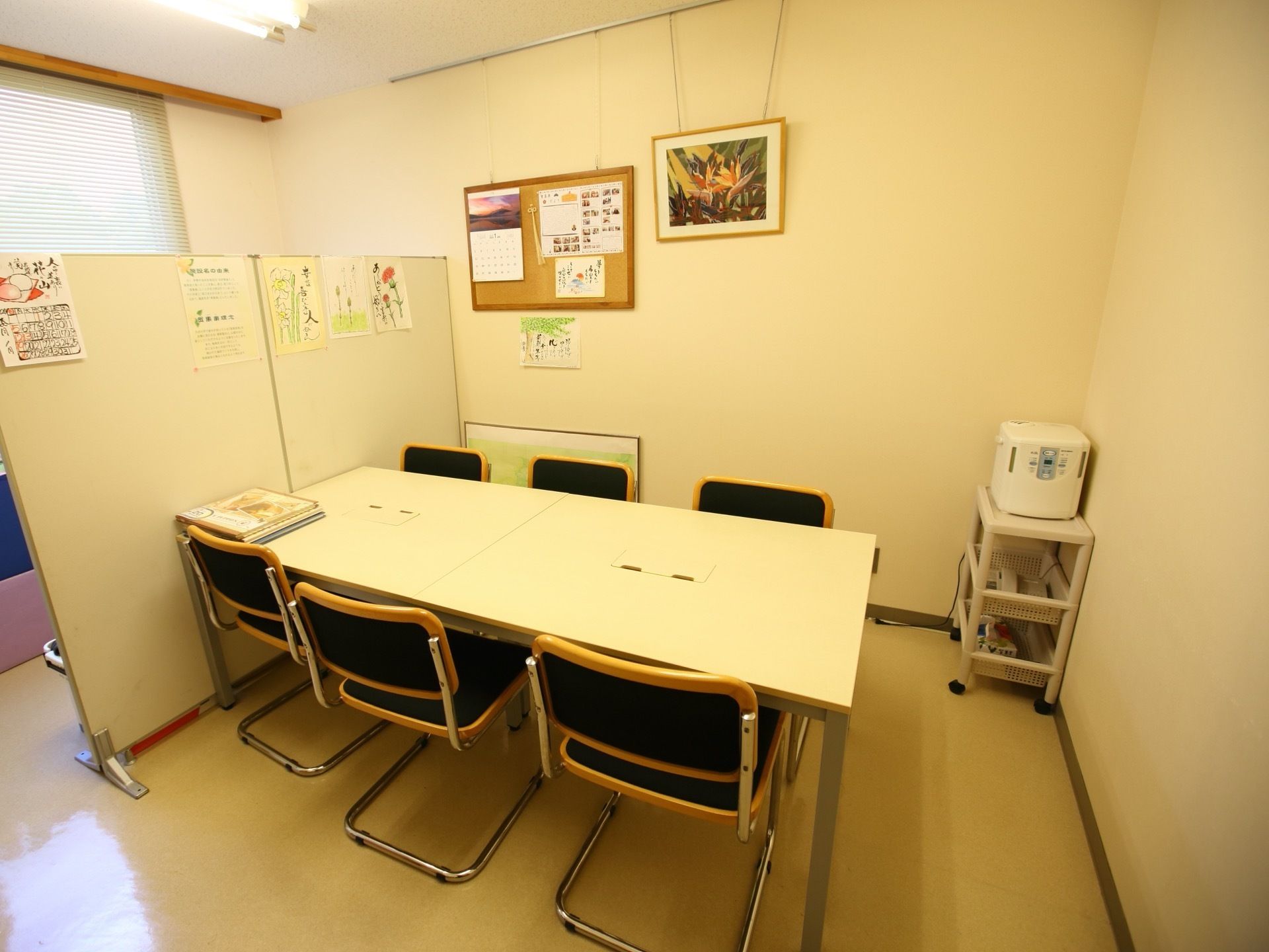 個室に6人掛けのテーブルがある。衝立や壁にカレンダーや花の絵を飾っている。相談室として使うことができる。