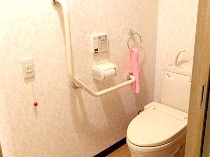 トイレはエル字型の手すりが設置されている。手洗い場もトイレについているので、タオルかけにはタオルがかけられている。