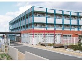 青いラインが書かれた白い大きな建物は各フロアにベランダがあり、玄関に車寄せがあり、庭もある。