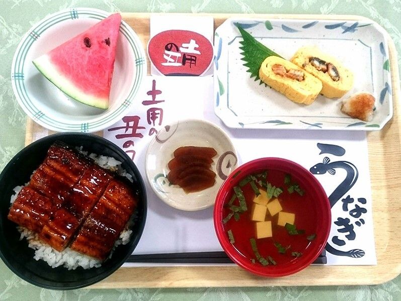 うな丼にウナギの切り身が入った卵焼き、吸い物、スイカのスライスなどが並んだ食事。