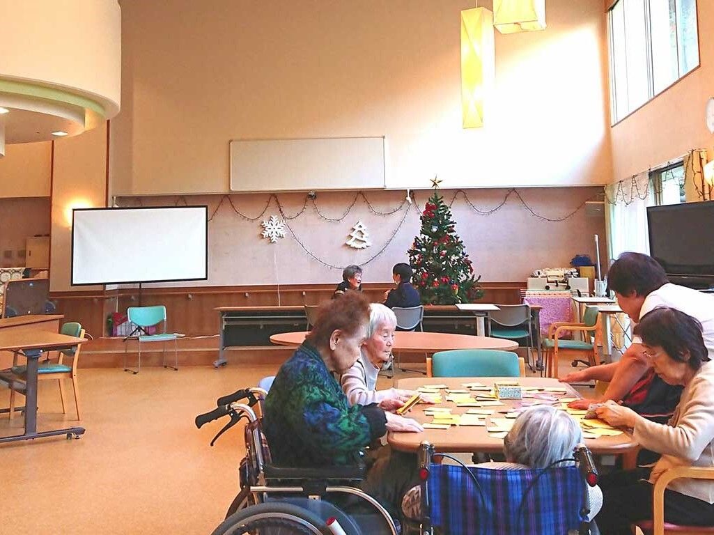 天井の高いホールでレクリエーションを楽しむ入居者たち。奥にはクリスマスツリーがある。