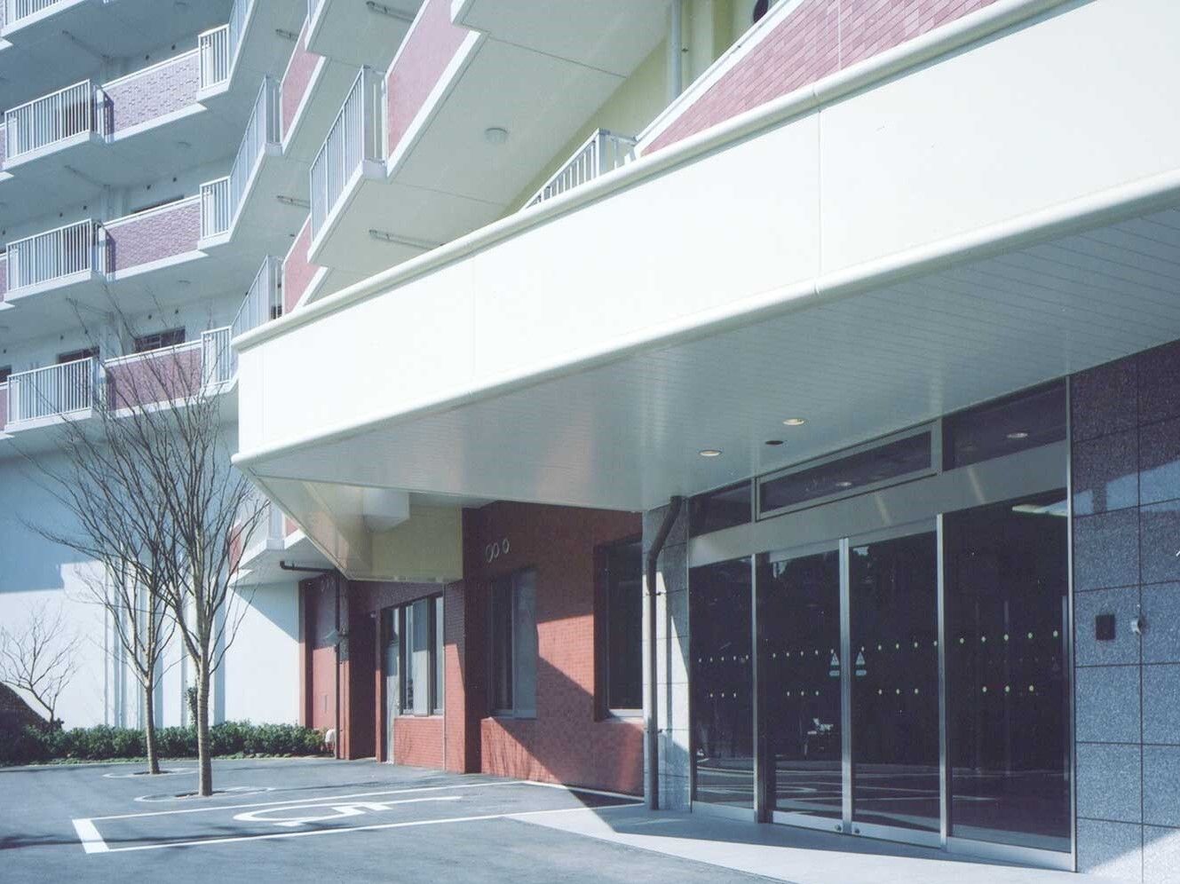 敷地内駐車場がある建物は白とピンクで玄関には自動ドアと車寄せが付いていて、日当たりのいい場所に建っている。