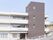 白とグレーの3階建ての建物。建物の周りには白いフェンスがあり、各フロアにベランダも付いている。