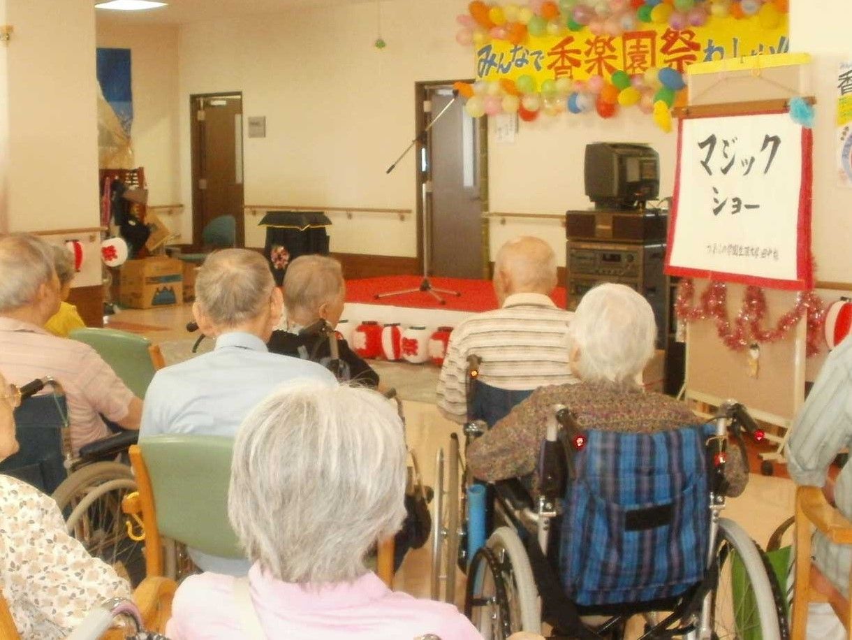 風船などで彩られたステージの横にはマジックショーと書かれたボードが飾られ、たくさんの入居者が観覧している。