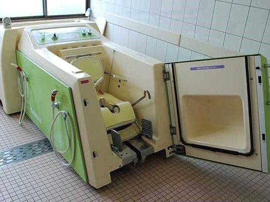 扉が開いている機械浴槽。入浴用の車いすのようなものが機械内部にセットされている。