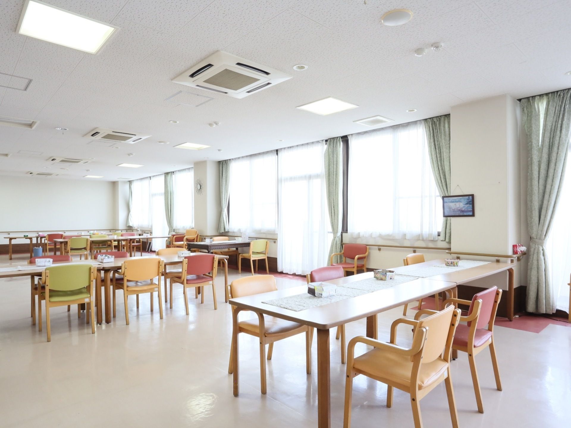 広い空間にはゆとりのある配置でテーブルセットが並べられている。大きな窓が設置されカーテンが設けられている。