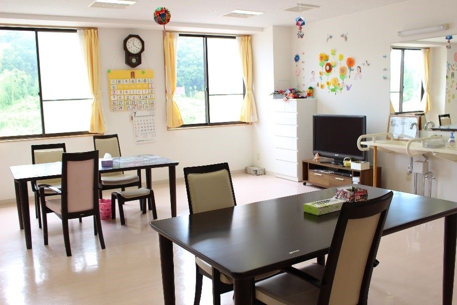 外の景色が望める明るい部屋である。ダイニングテーブルと背もたれのある椅子のセットが数組置かれている。手すりの付いた洗面台が設置されている。