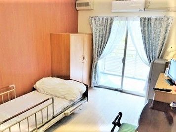 布団がセットされたベッドがある居室。カーテンが付いた窓は大きく、部屋にはテーブルセットもある。